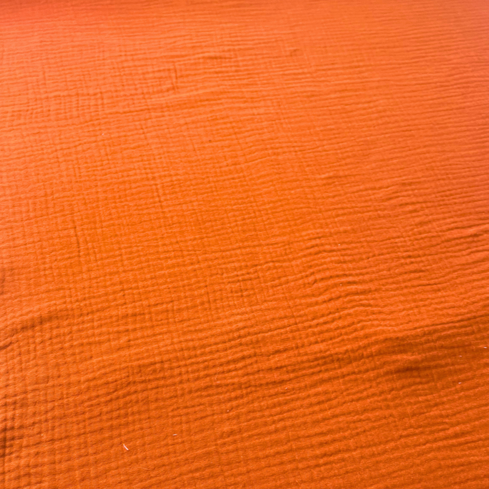 Flat lay of burnt orange plain double gauze fabric draped to show featherlight 125gsm weight and fluid drape — GOTS certified organic cotton perfect for handmade summer and autumn dresses, blouses and children's playsuits