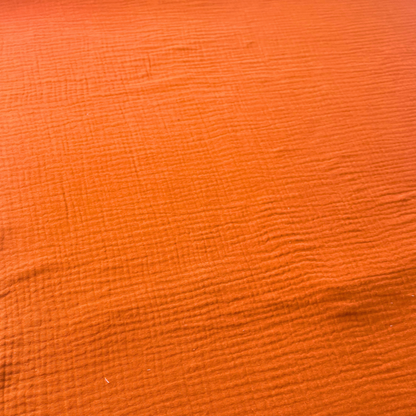 Flat lay of burnt orange plain double gauze fabric draped to show featherlight 125gsm weight and fluid drape — GOTS certified organic cotton perfect for handmade summer and autumn dresses, blouses and children's playsuits