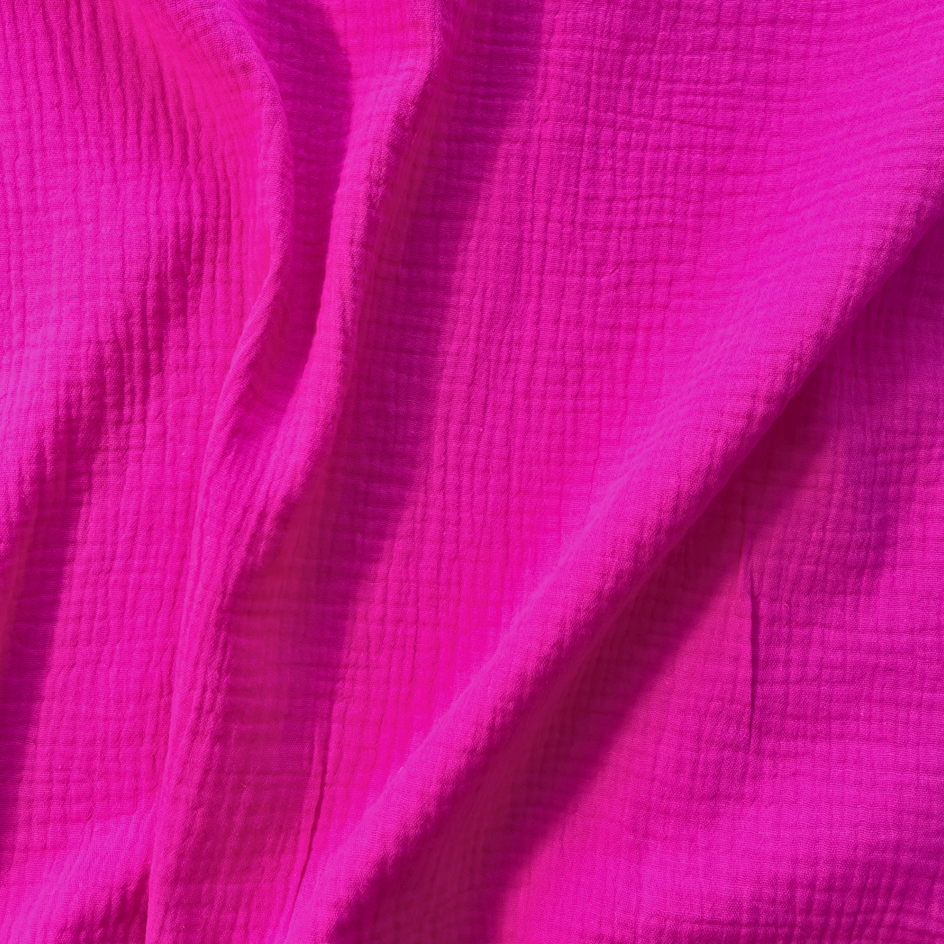 Flat lay of cerise pink plain double gauze fabric draped to show featherlight 125gsm weight and fluid drape — GOTS certified organic cotton perfect for handmade summer dresses, blouses and children's playsuits