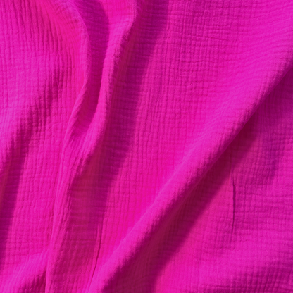 Flat lay of cerise pink plain double gauze fabric draped to show featherlight 125gsm weight and fluid drape — GOTS certified organic cotton perfect for handmade summer dresses, blouses and children's playsuits