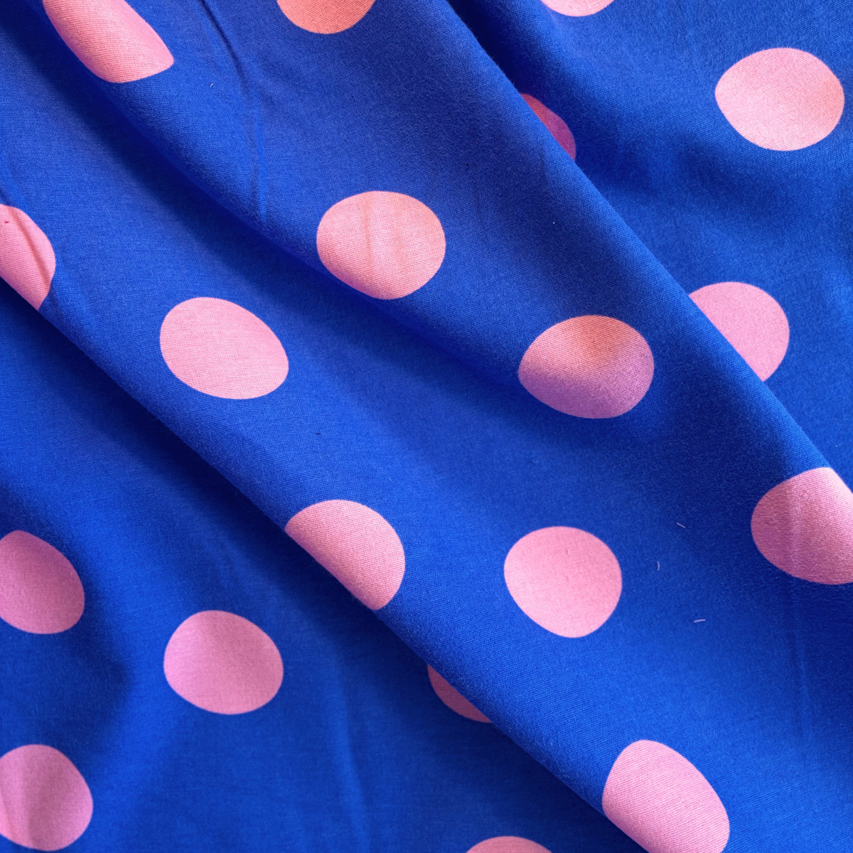 Close-up of cobalt blue flannel fabric with large bold pink polka dots showing soft brushed woven texture — 165gsm Oeko-Tex Standard 100 certified slow fashion dressmaking fabric UK