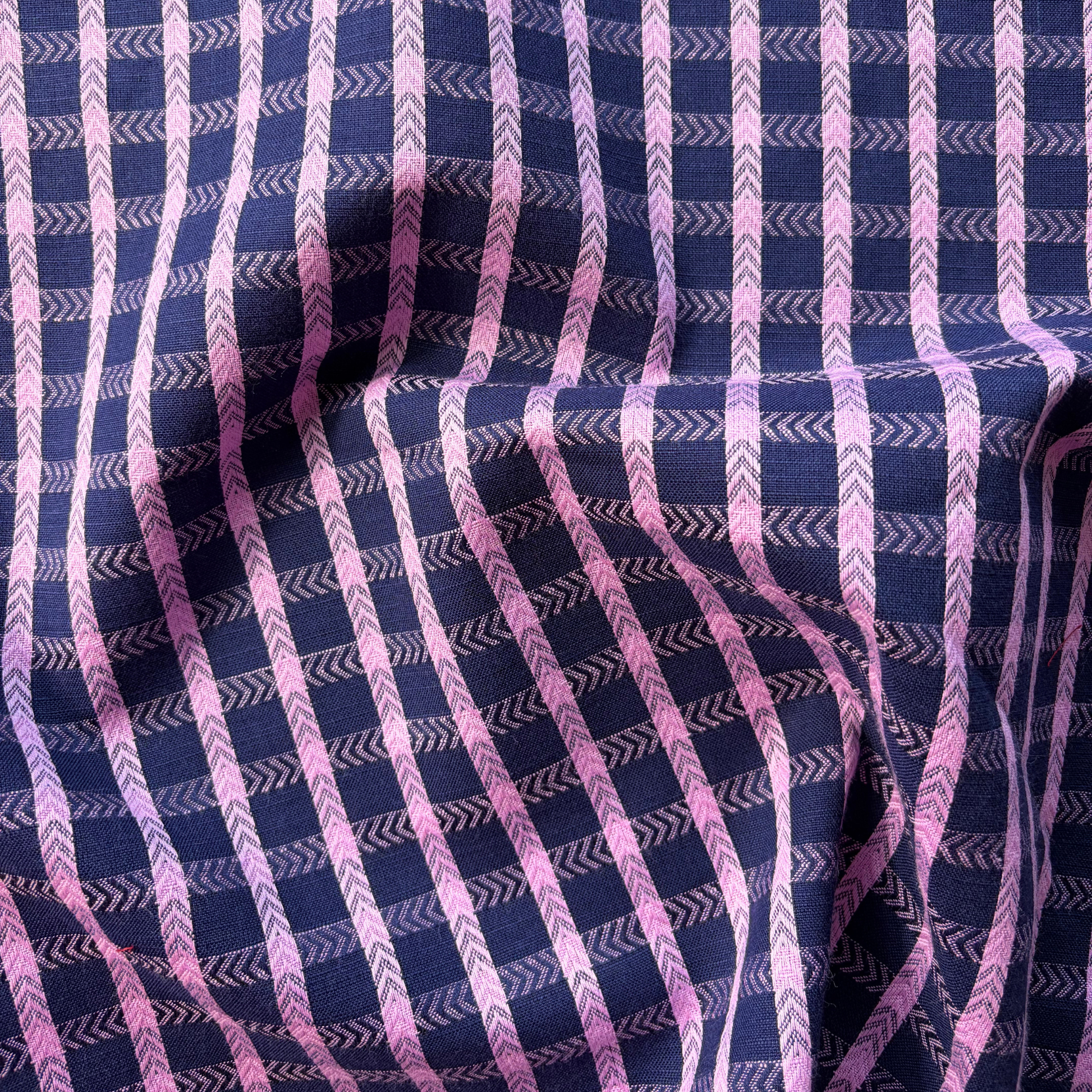 A close-up of a draped fabric with a navy blue base, decorated with vertical pink stripes and chevron patterns.