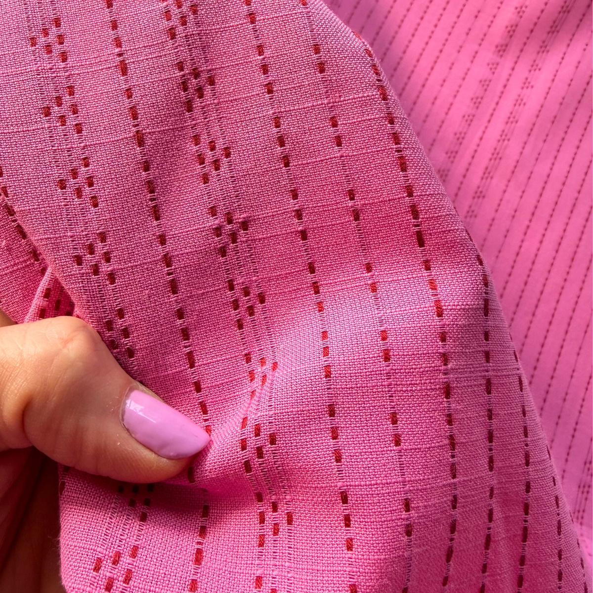 Close-up of bright pink and lilac yarn dyed dobby stripe woven cotton fabric showing raised vertical dot and dash stripe texture — 135gsm slow fashion dressmaking fabric UK