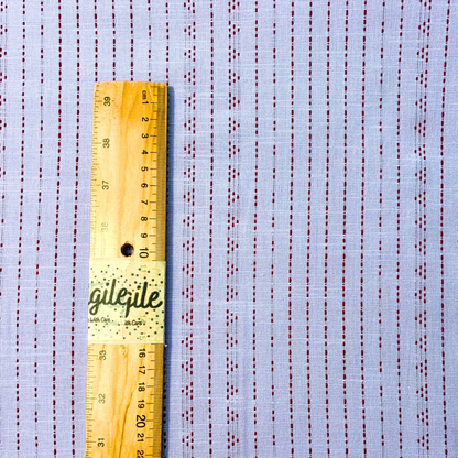 Close-up of lilac and burgundy yarn dyed dobby stripe woven cotton fabric showing raised vertical dot and dash stripe texture — 135gsm slow fashion autumnal dressmaking fabric UK