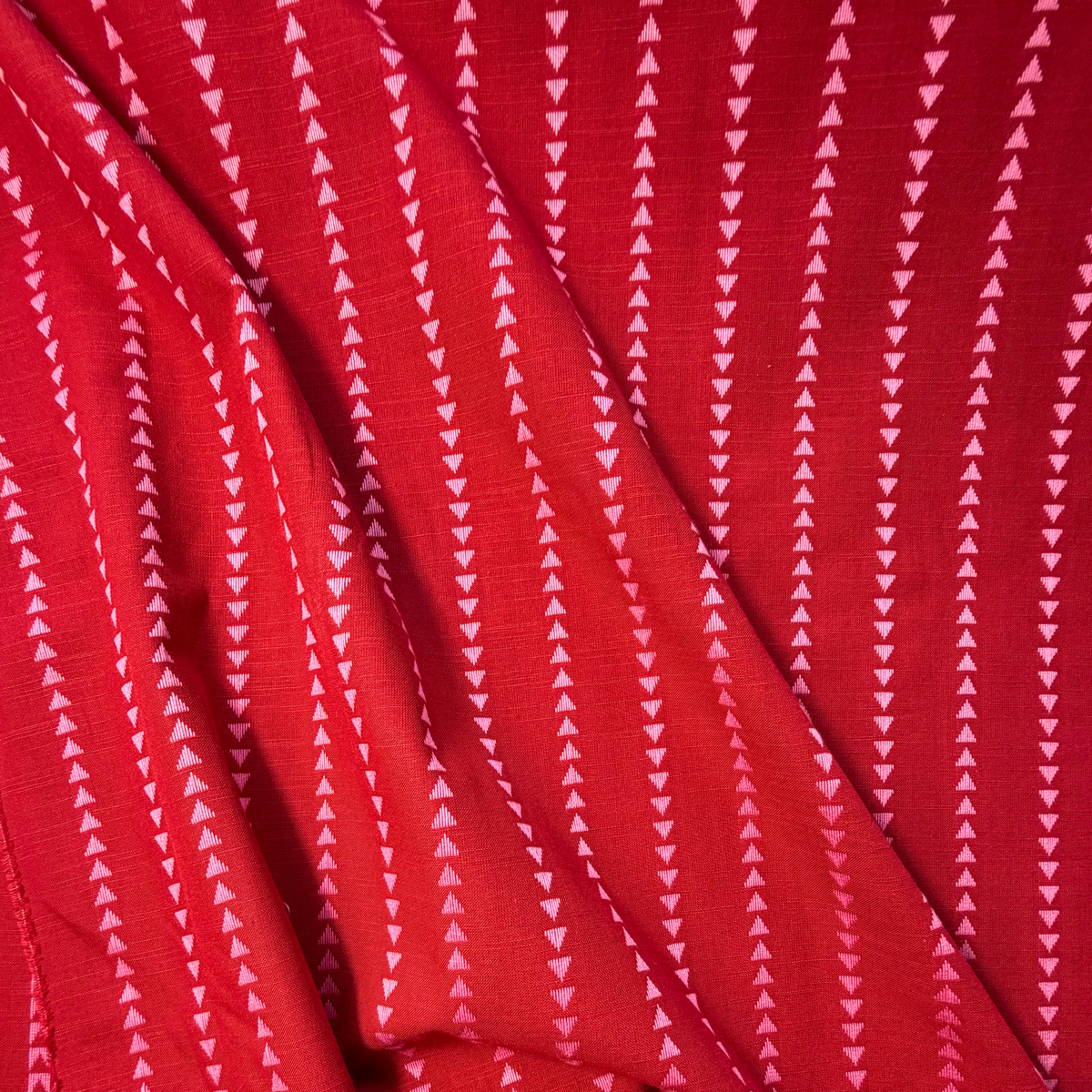 Close-up of burnt red and pink yarn dyed dobby triangle stripe woven cotton fabric showing raised vertical mini triangle texture — reversible cut direction 135gsm slow fashion dressmaking fabric UK