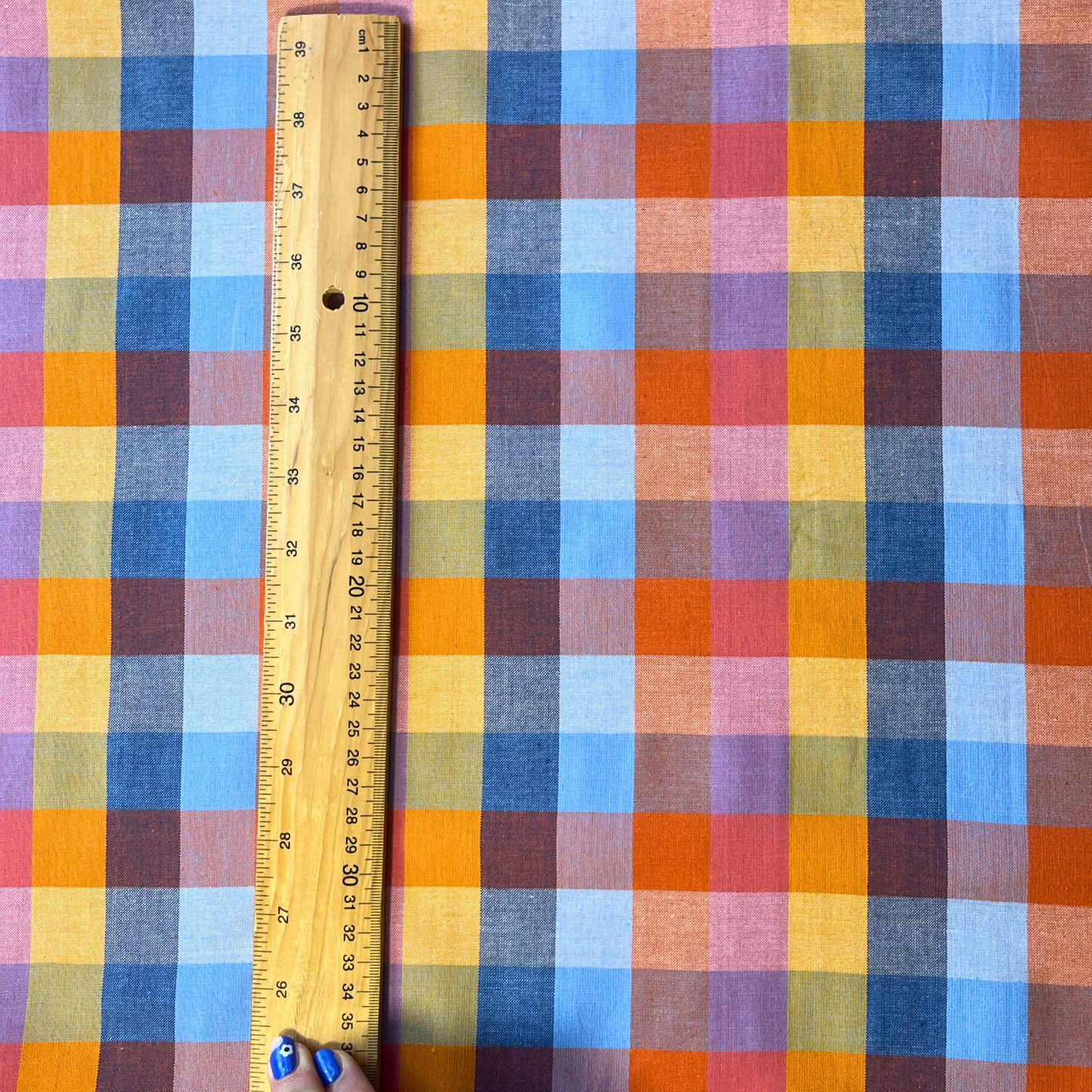 Flat lay of Fableism Cornucopia Happy Checkers multicolour gingham cotton fabric draped to show 135gsm natural drape and 110cm width — yellow orange blue and pink check perfect for handmade dresses skirts and trousers