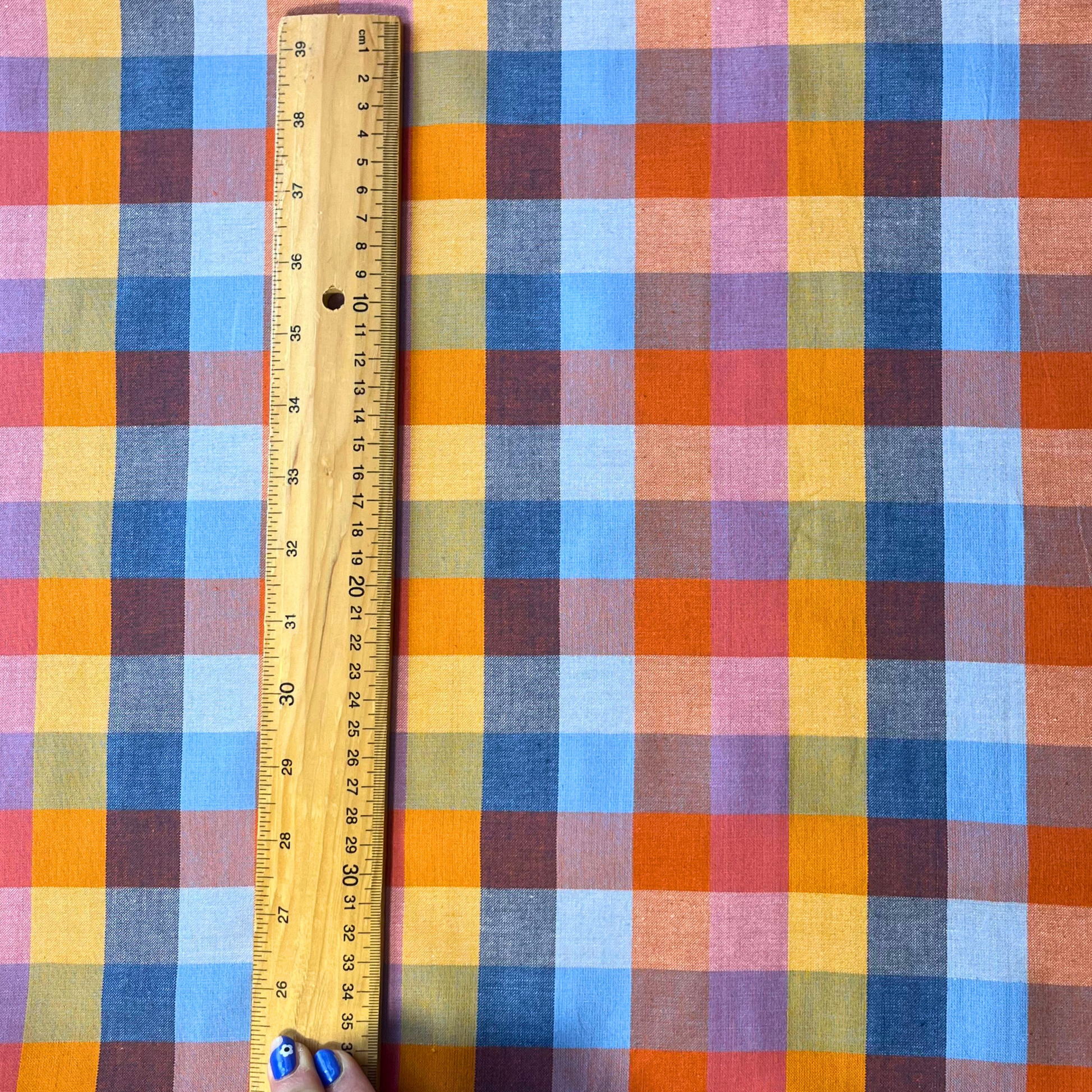 Flat lay of Fableism Cornucopia Happy Checkers multicolour gingham cotton fabric draped to show 135gsm natural drape and 110cm width — yellow orange blue and pink check perfect for handmade dresses skirts and trousers