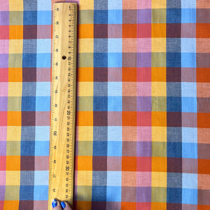 Flat lay of Fableism Cornucopia Happy Checkers multicolour gingham cotton fabric draped to show 135gsm natural drape and 110cm width — yellow orange blue and pink check perfect for handmade dresses skirts and trousers
