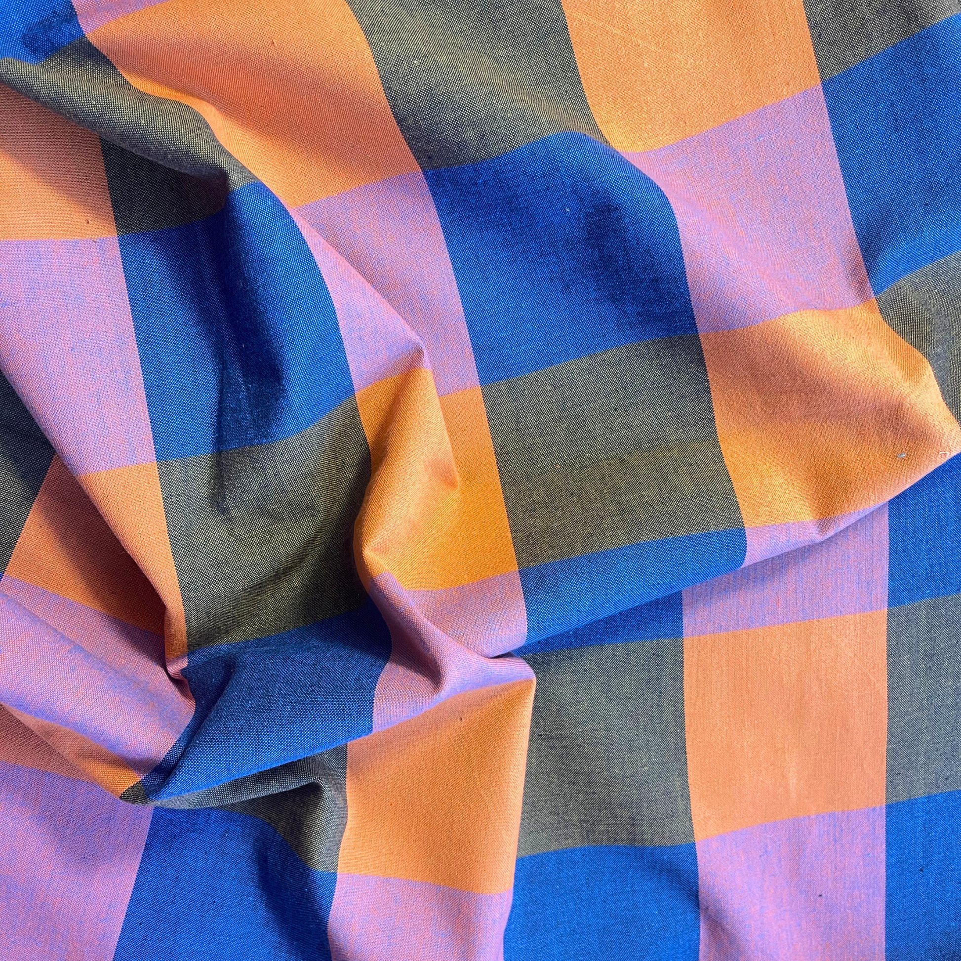 Close-up of Fableism Fine and Dandy Happy Checkers woven cotton fabric showing bold 7.5cm multicolour check in cobalt blue orange khaki and lilac — lightweight 135gsm dressmaking fabric ideal for slow fashion sewing