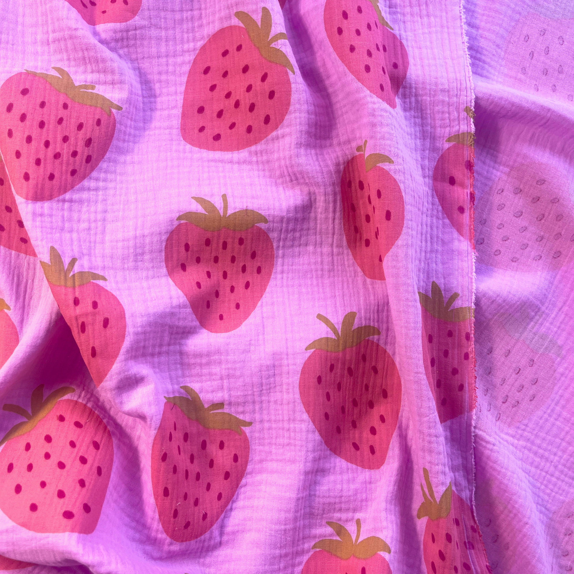 Pink double gauze strawberry print fabric folded to show soft two-layer cotton construction and large scale washed fruit motifs approximately 9x10cm — featherlight breathable fabric ideal for handmade blouses, summer dresses, children's playsuits and baby muslins