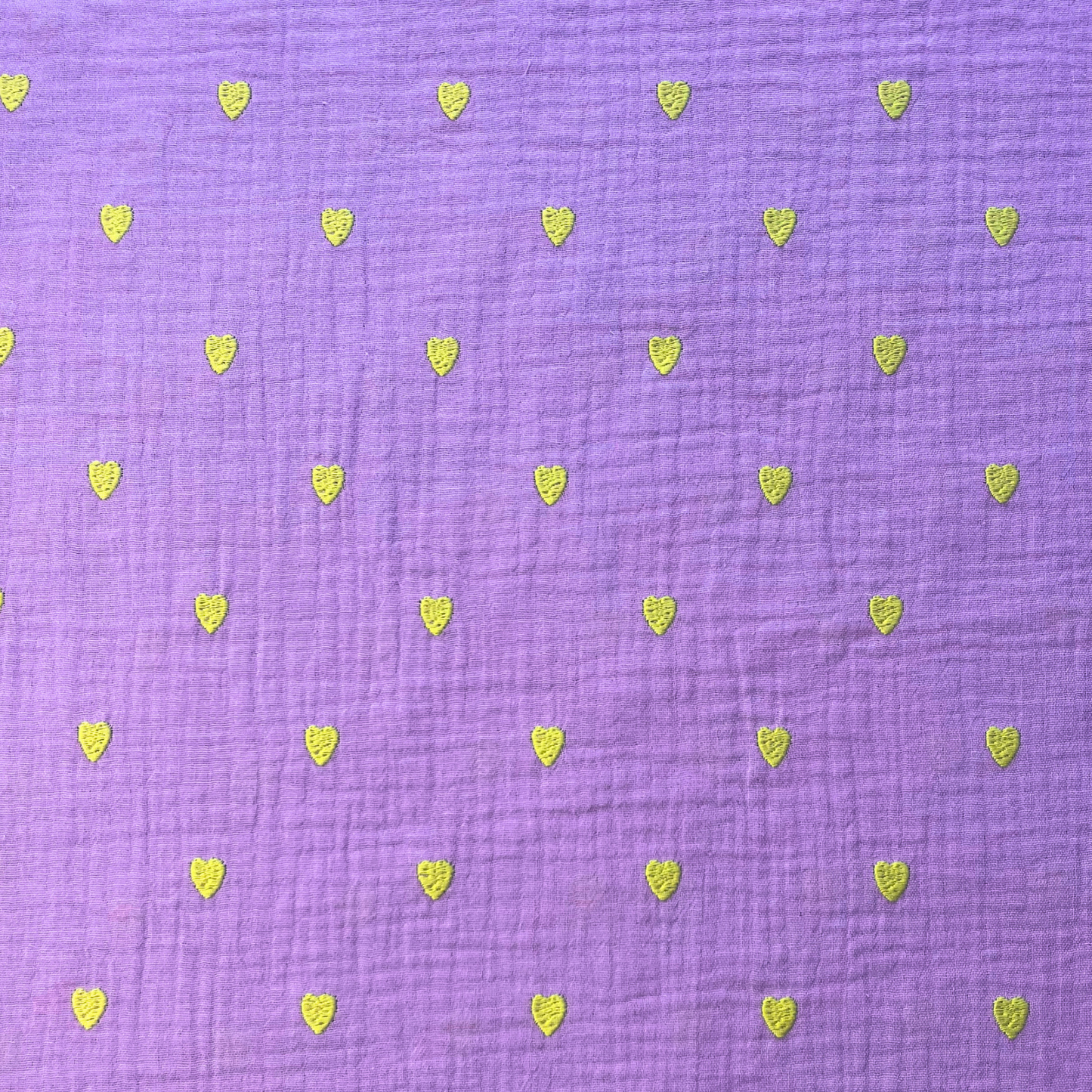 Close-up of soft lavender double gauze fabric showing tiny scattered neon yellow embroidered hearts with tactile stitched texture — Oeko-Tex certified 140gsm 100% cotton woven ideal for handmade children's dresses, baby swaddles and adult blouses