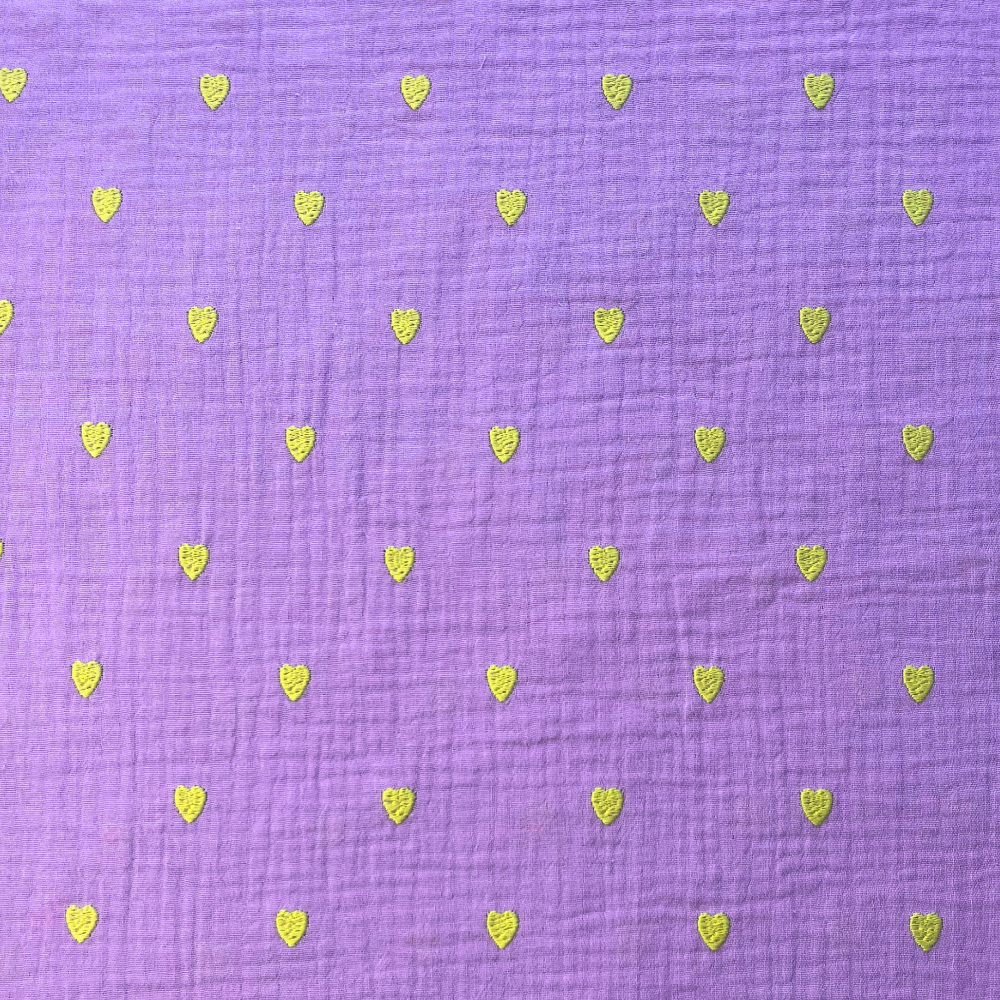 Close-up of soft lavender double gauze fabric showing tiny scattered neon yellow embroidered hearts with tactile stitched texture — Oeko-Tex certified 140gsm 100% cotton woven ideal for handmade children's dresses, baby swaddles and adult blouses