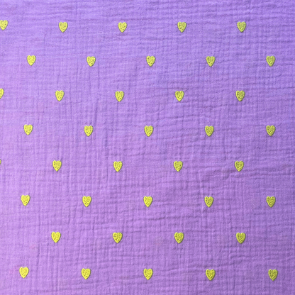 Close-up of soft lavender double gauze fabric showing tiny scattered neon yellow embroidered hearts with tactile stitched texture — Oeko-Tex certified 140gsm 100% cotton woven ideal for handmade children's dresses, baby swaddles and adult blouses