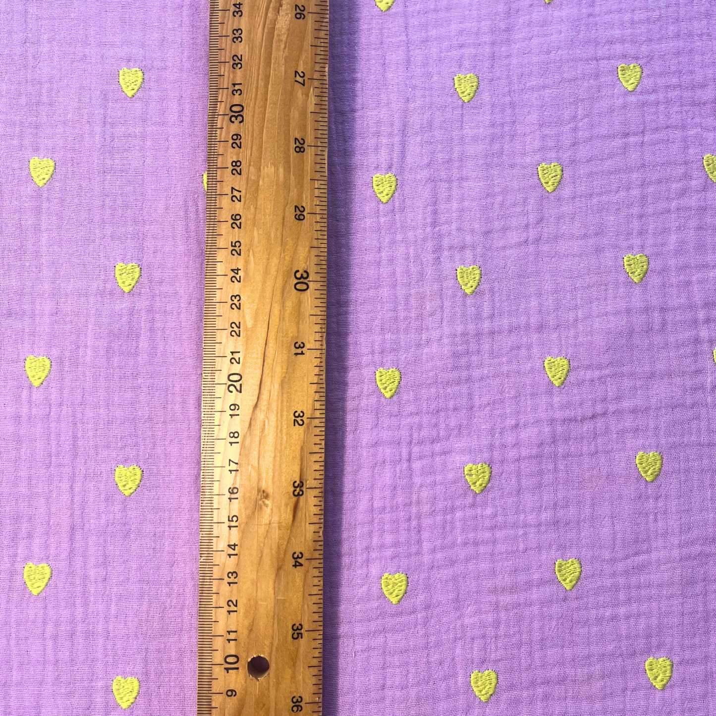 Close-up of soft lavender double gauze fabric showing tiny scattered neon yellow embroidered hearts with tactile stitched texture — Oeko-Tex certified 140gsm 100% cotton woven ideal for handmade children's dresses, baby swaddles and adult blouses