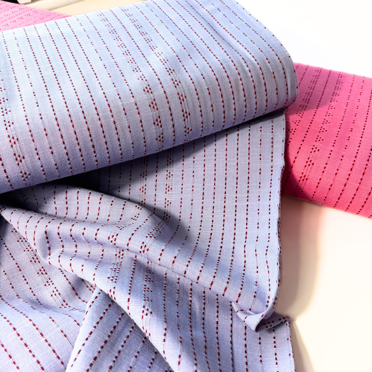 Lilac burgundy dobby stripe cotton fabric flat lay showing 135gsm natural drape and generous 145cm width — yarn dyed vertical dot dash woven stripe perfect for handmade blouses dresses and transitional autumn makes