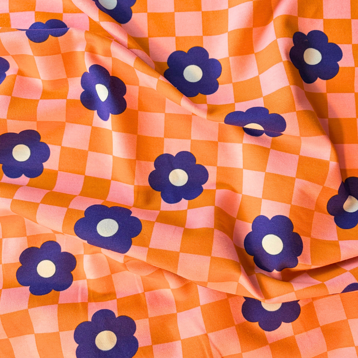 Close-up of orange pink checkerboard sweatshirting with medium blue retro bloom print showing soft brushed interior — 225gsm cotton elastane Oeko-Tex Standard 100 certified stretch fabric UK