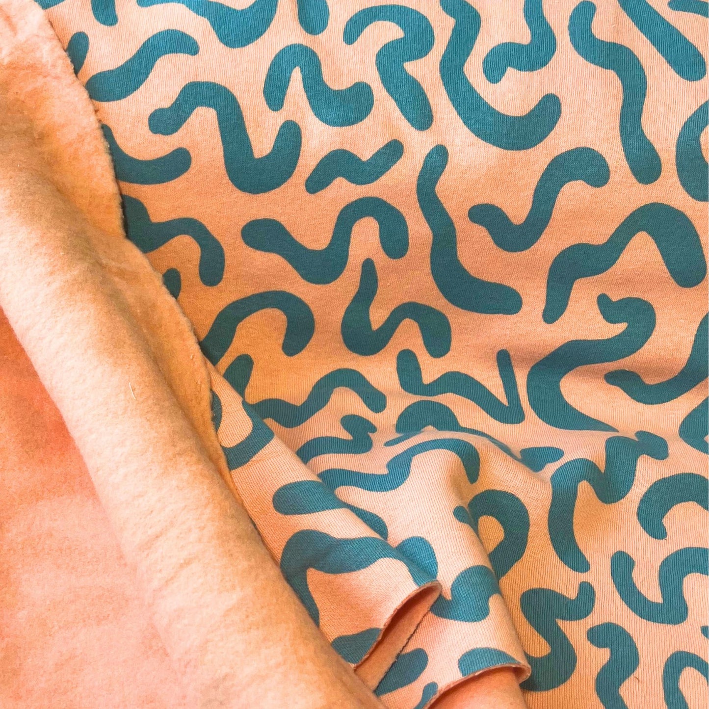 Peachy pink brushed back fabric with teal squiggles, photographed to show texture and softness.