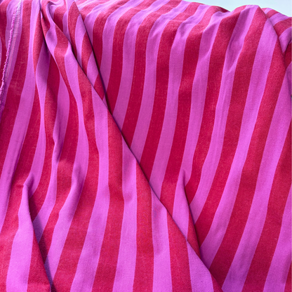 Red and cerise pink vertical stripe yarn dyed cotton fabric folded to show woven construction — 2.2cm stripe 145cm wide Oeko-Tex certified lightweight dressmaking fabric for blouses pinafores and summer dresses