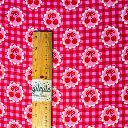 Red pink cherry gingham needlecord fabric flat lay showing 125gsm drape and 112cm width, cotton corduroy with repeating cherry print perfect for handmade pinafores trousers and jackets