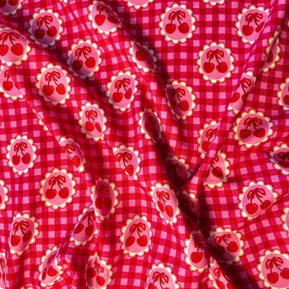 Red and pink gingham cherry needlecord fabric folded to show soft corduroy ridges and circular cherry motifs, 112cm wide cotton corduroy for handmade skirts bags and soft furnishings