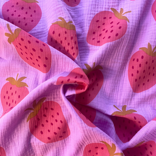 Close-up of pink double gauze fabric showing large scale washed strawberry print approximately 9x10cm per motif — soft two-layer Oeko-Tex certified 100% cotton woven ideal for handmade children's dresses, baby swaddles and adult blouses