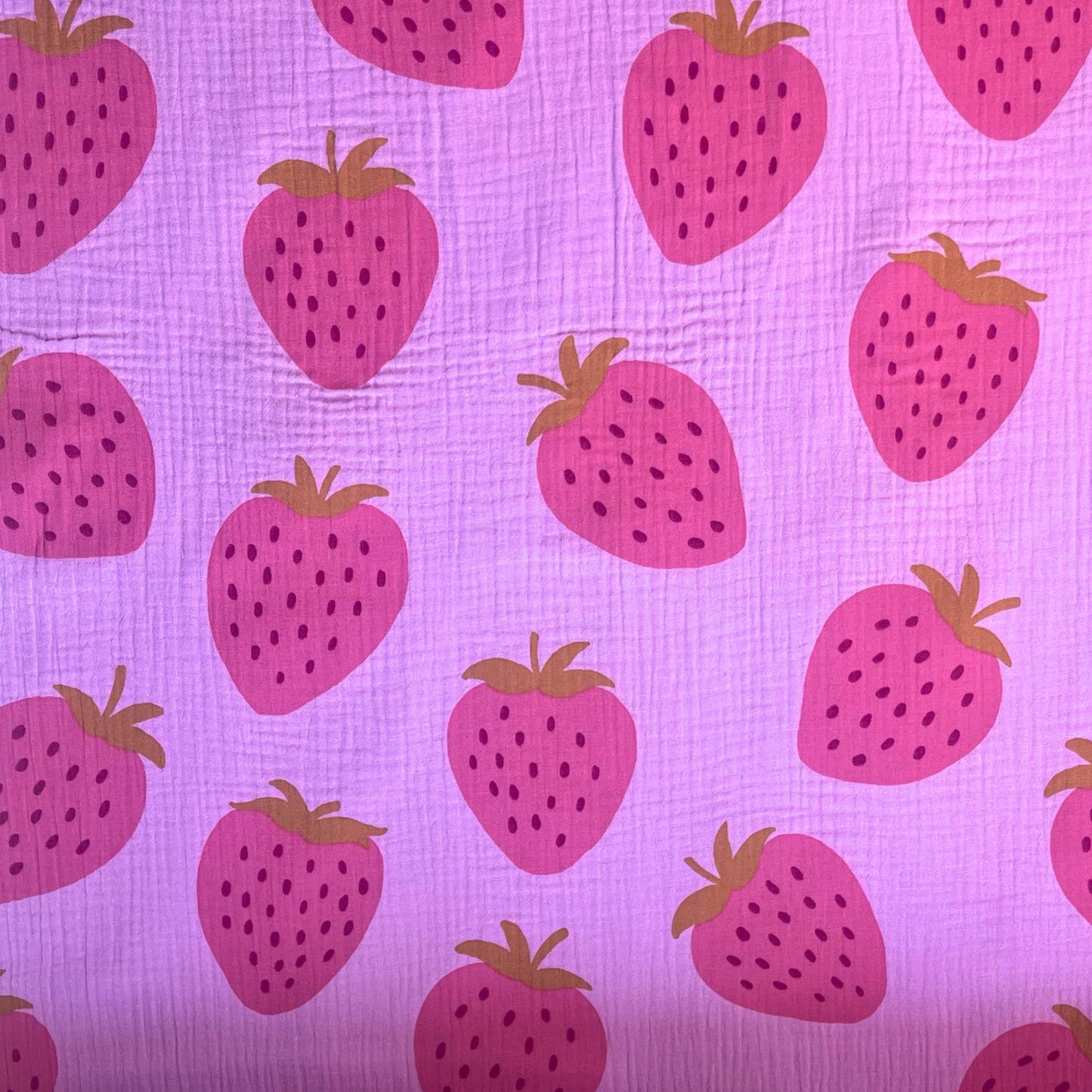 Flat lay of pink strawberry print double gauze fabric draped to show featherlight 125gsm weight and soft two-layer construction — large scale washed fruit print on pink base perfect for handmade summer dresses, playsuits and children's clothing