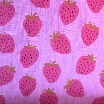 Flat lay of pink strawberry print double gauze fabric draped to show featherlight 125gsm weight and soft two-layer construction — large scale washed fruit print on pink base perfect for handmade summer dresses, playsuits and children's clothing