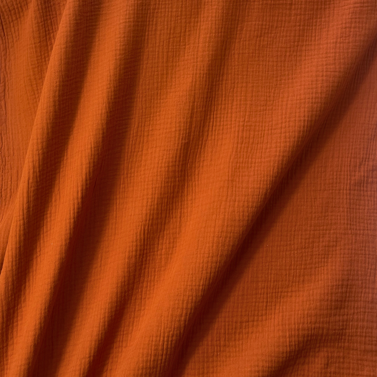 Flat lay of terracotta plain double gauze fabric draped to show featherlight 125gsm weight and fluid drape — GOTS certified organic cotton perfect for handmade summer dresses, blouses and children's playsuits