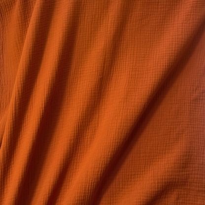 Flat lay of terracotta plain double gauze fabric draped to show featherlight 125gsm weight and fluid drape — GOTS certified organic cotton perfect for handmade summer dresses, blouses and children's playsuits