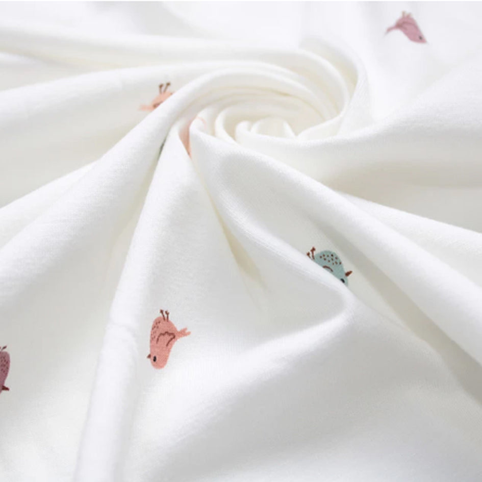 Flat lay of white miniature birds jersey fabric draped to show 200gsm weight and stretch — delicate nature-inspired bird print in soft muted tones perfect for handmade baby gifts and children's slow fashion sewing