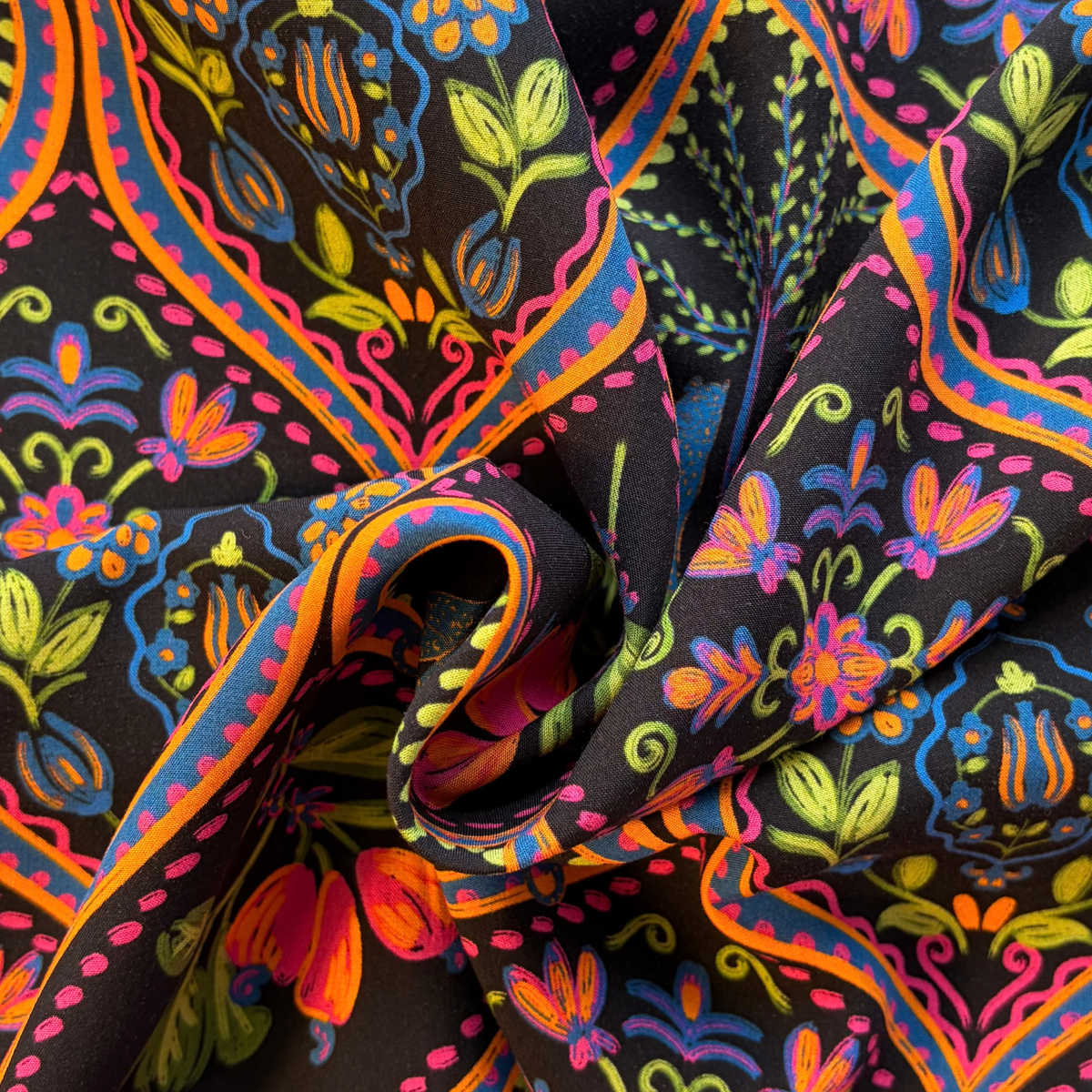 Close-up of black viscose fabric showing wild tropical digital print with leopards palms and botanical motifs in vivid pink purple blue green and orange — 110gsm fluid woven slow fashion dressmaking fabric UK