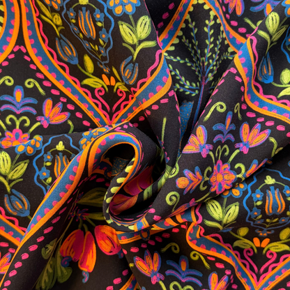 Close-up of black viscose fabric showing wild tropical digital print with leopards palms and botanical motifs in vivid pink purple blue green and orange — 110gsm fluid woven slow fashion dressmaking fabric UK