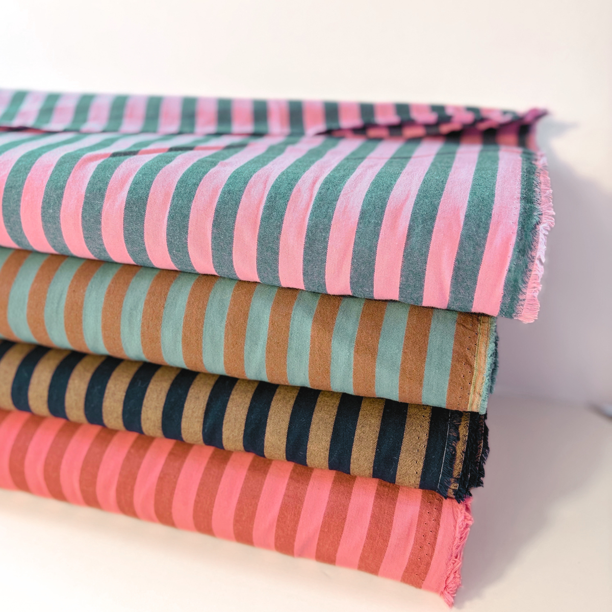 Washed pink and petrol blue yarn dyed stripe woven cotton fabric folded to show soft stripe definition — 1.25cm stripe 145cm wide Oeko-Tex certified lightweight dressmaking fabric for blouses shirts and summer dresses